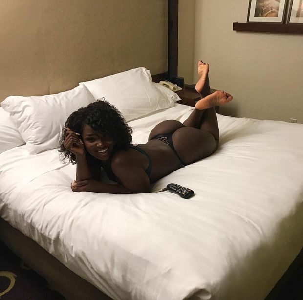 sexy dark skinned black woman laying barefoot on bed smiling with great ass in thong