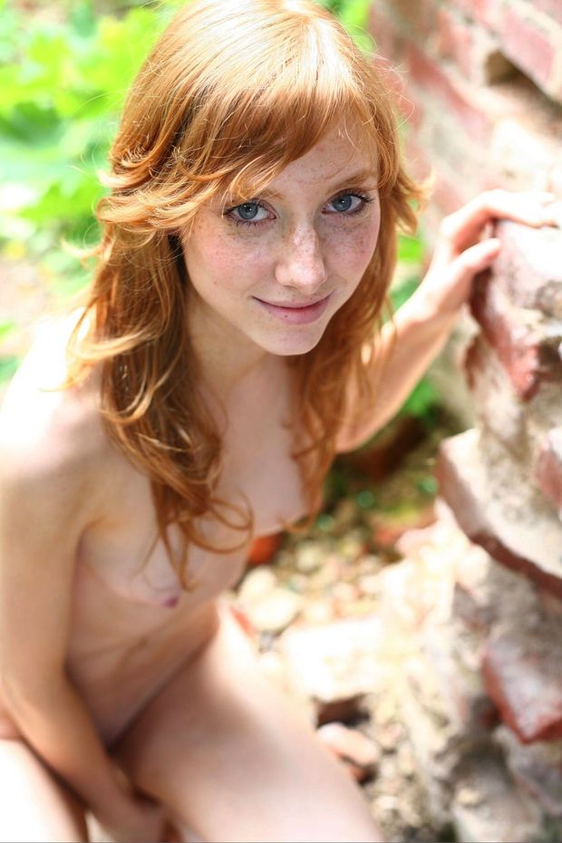 A cute little wood nymph with a freckled face smiles rays of sunshine up at you from below as she kneels her naked body atop a bed of cedar