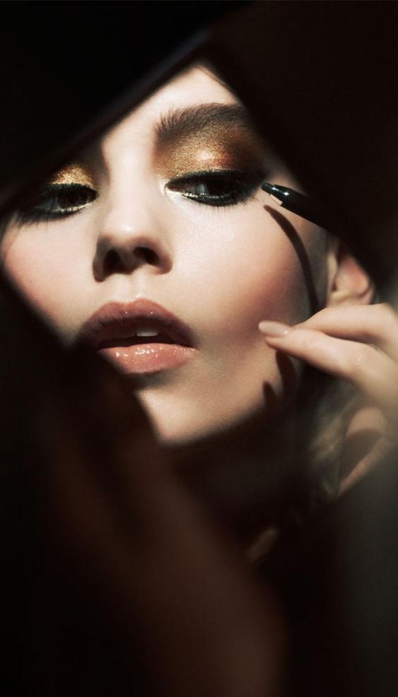 Woman with golden eyeshadow applying dark khol