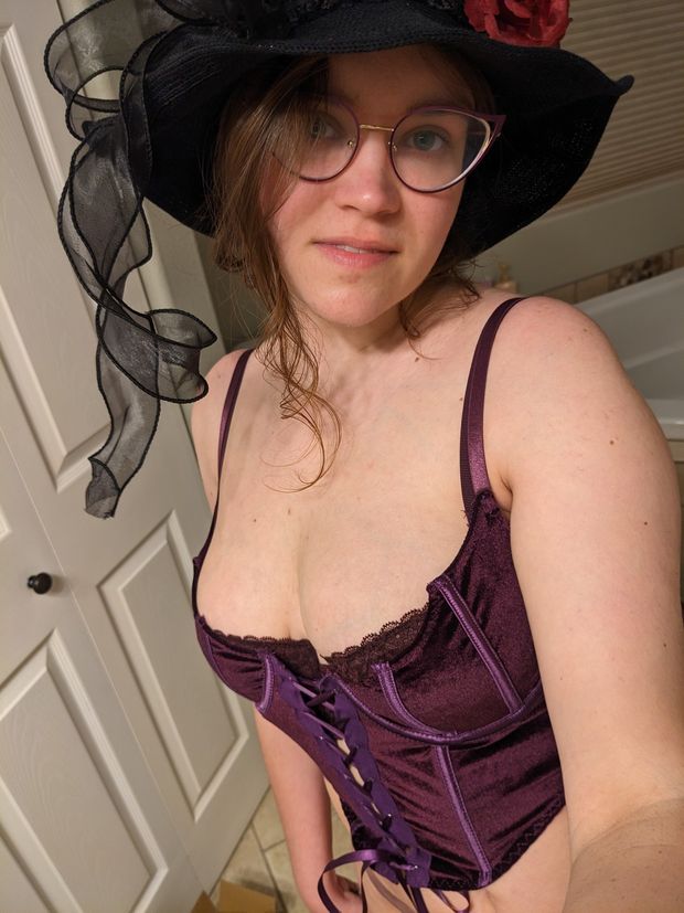 Aluvandria in a purple corset, witch hat, and glasses